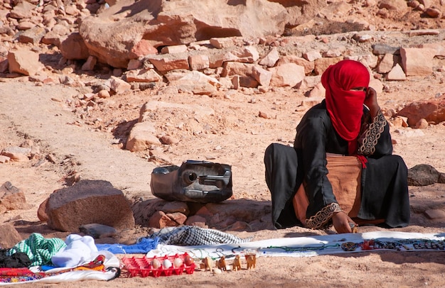 La donna beduina con la faccia coperta si siede sulla sabbia nel deserto