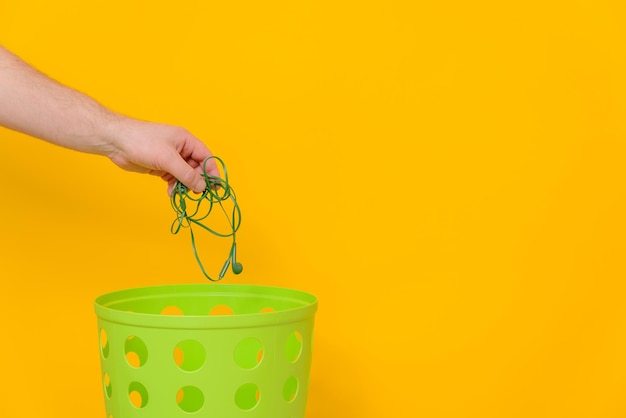 Bedrade hoofdtelefoons worden in een groene vuilnisbak gegooid voor verwijdering en recycling