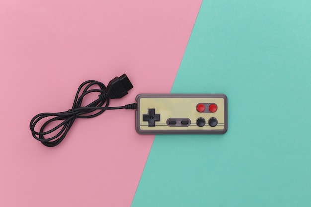 Bedrade retro gamepad en joystick met gewikkelde kabel op roze blauwe achtergrond. Videospelletjes, gamen. Bovenaanzicht