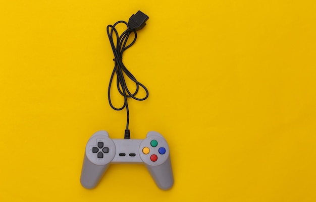 Bedrade retro gamepad (joystick) met gewikkelde kabel op gele achtergrond. Videospelletjes, gamen. Bovenaanzicht