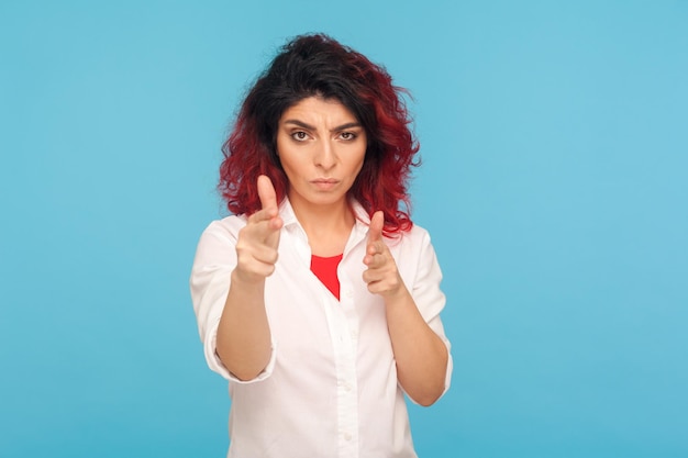 Bedreiging tot moord portret van gevaarlijke hipster vrouw met mooie rood haar vinger geweren wijzend naar camera hand pistolen gebaar maken gericht op het doden van indoor studio shot geïsoleerd op blauwe achtergrond