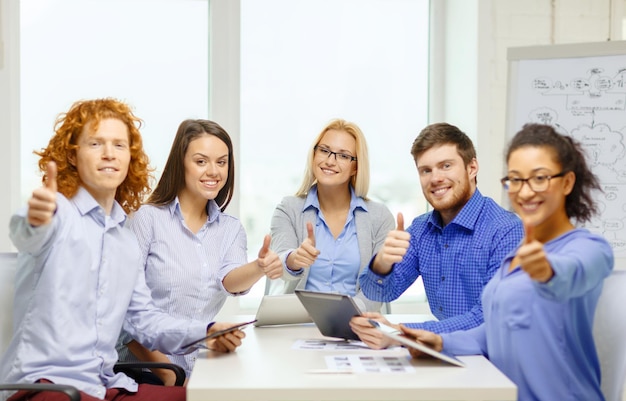 bedrijf, kantoor, gebaar en startup concept - glimlachend creatief team met tafel-pc-computers en papieren die duimen opdagen op kantoor