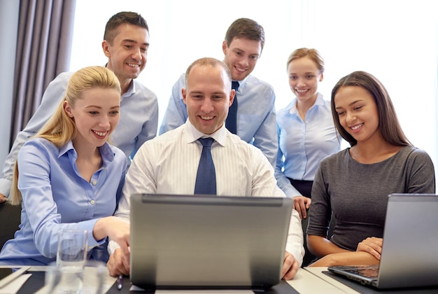 bedrijf, mensen, technologie en communicatieconcept - glimlachend business team met laptopcomputer die videoconferentie maakt op kantoor