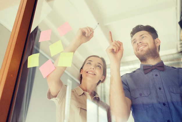 bedrijf, opstarten, planning, management en mensenconcept - gelukkig creatief team dat iets schrijft of tekent op een leeg kantoorglasbord