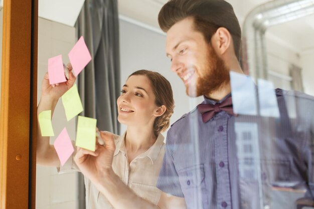 bedrijf, opstarten, planning, management en mensenconcept - gelukkig creatief team schrijven op stickers op kantoorglasbord