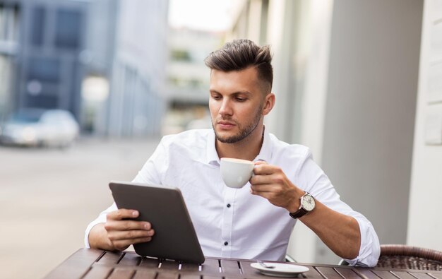 bedrijf, technologie en mensen concept - jonge man met tablet pc computer en koffiekop in het stadsstraat café