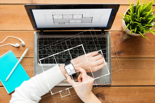 bedrijfs-, architectuur-, mensen- en technologieconcept - close-up van vrouw met slim horloge en laptopcomputer op houten tafel met blauwdrukprojectie