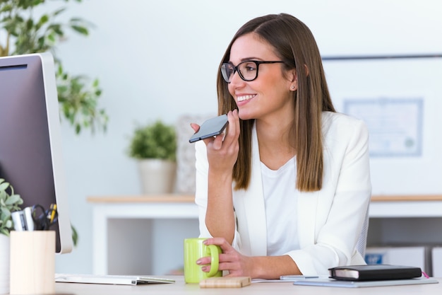 Bedrijfs jonge vrouw die haar mobiele telefoon in het bureau met behulp van.