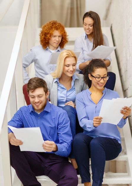 bedrijfs-, kantoor- en startup-concept - glimlachend creatief team met papieren en afhaalkoffie op de trap