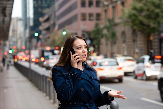 Bedrijfs vrouw die op mobiel spreekt die onderaan stadsstraat loopt. Halve lengte foto.