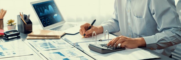 Bedrijfsauditor berekent budget met rekenmachine op kantoor met BI-dashboard op laptopscherm Professionele accountant van accountantskantoor analyseert financieel document voor winstgevend inkomen Insight