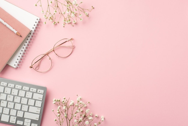 Bedrijfsconcept Bovenaanzicht foto van werkruimte toetsenbord planners potlood stijlvolle bril en witte gypsophila bloemen op geïsoleerde pastelroze achtergrond met copyspace