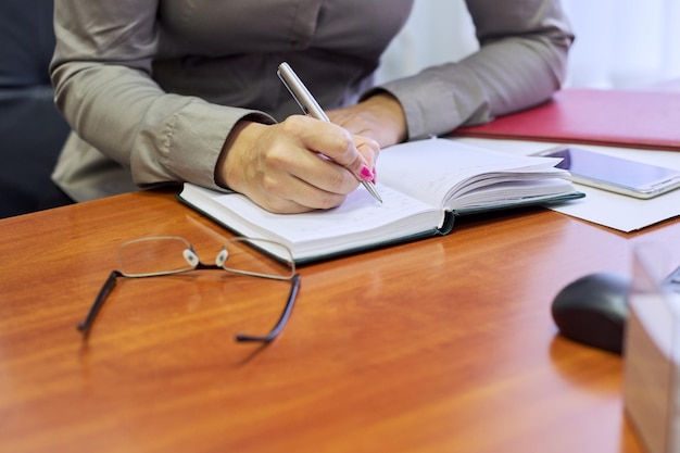 Bedrijfsconcept, close-up vrouwelijke handen schrijven in een zakelijke notebook, werkplek desktop op kantoor