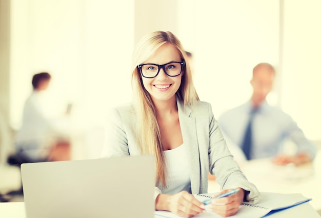 bedrijfsconcept - lachende vrouw met laptop, documenten en pen in office