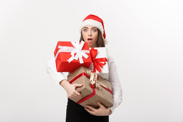 Bedrijfsconcept mooie jonge blanke zakenvrouw met kerstmuts met veel geschenkdozen met verrassende gezichtsuitdrukking