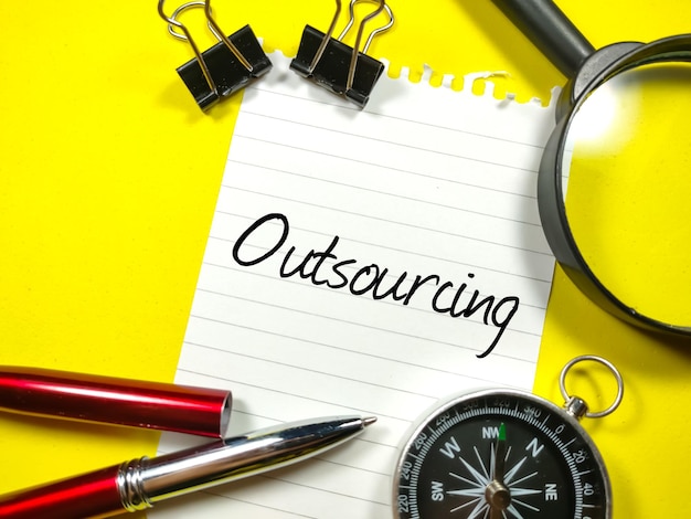 BedrijfsconceptTekst Outsourcing schrijven op briefpapier met paperclipspenvergrootglas en kompas op gele achtergrond
