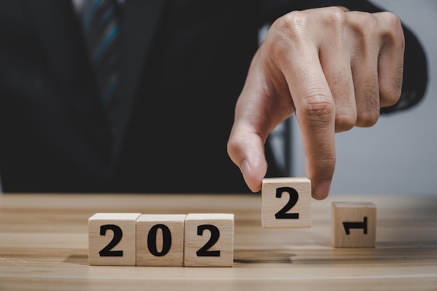 Bedrijfsjaar. zakenmanhand die houten kubus zet met nummerverandering van 2021 tot 2022, nieuwjaarsfelicitatie, kwartaalrapport, businessplan, aftellen tot 2022, doel en doelplanningsconcept