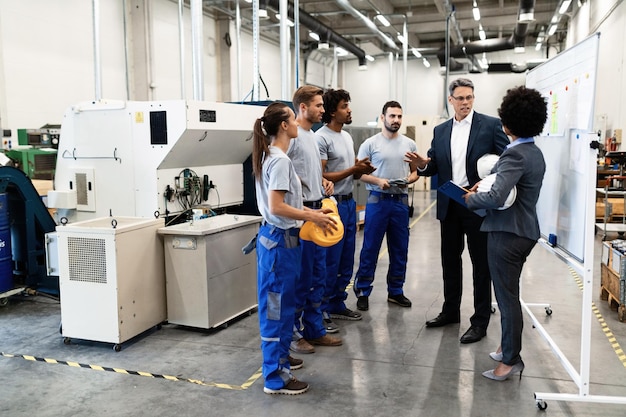 Bedrijfsmanager in gesprek met een groep industriële arbeiders tijdens een personeelsvergadering in een fabriek