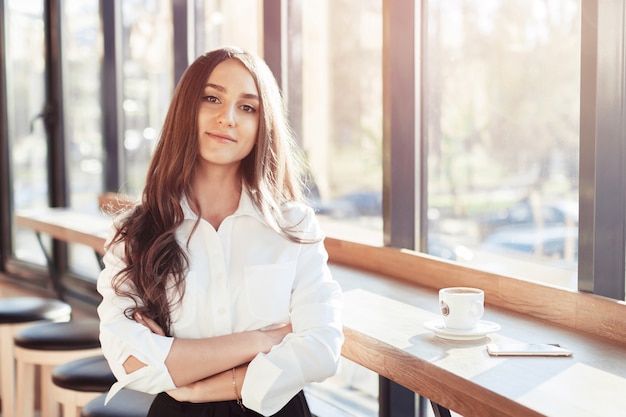 Bedrijfsmeisje in witte blouse in koffie die en cam glimlachen bekijken