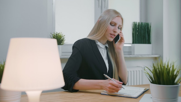 Bedrijfsvrouw die op smartphone in bureau spreken.