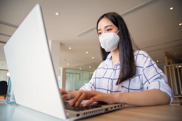 Bedrijfsvrouw die van huis werken die beschermend masker dragen en laptop computer met behulp van. Corona-uitbraak