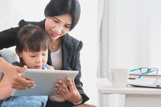 Bedrijfsvrouw en meisje speelspel op tablet in huisbureau