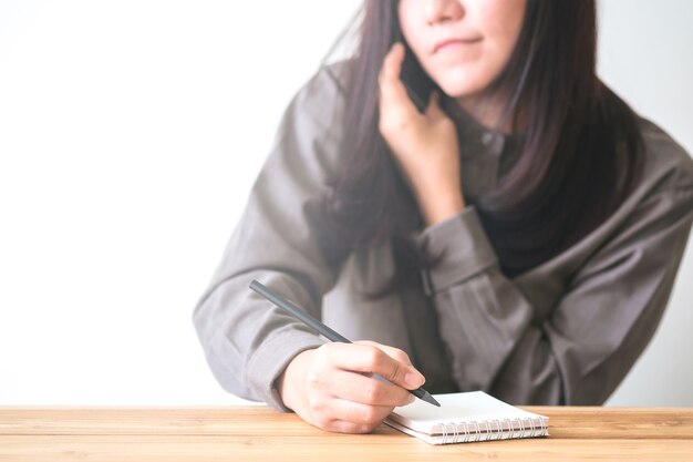 Bedrijfsvrouw gebruikend telefoon en schrijvend notitieboekje