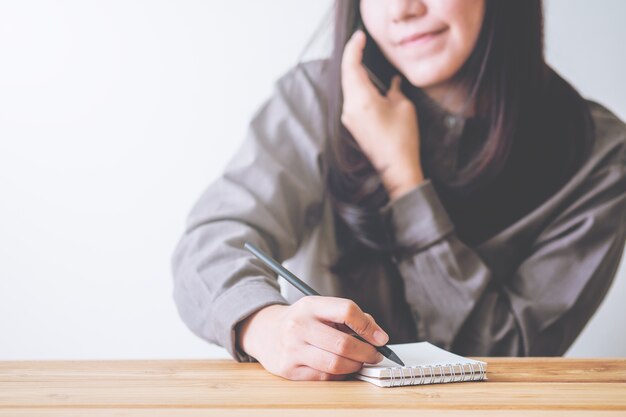 Bedrijfsvrouw gebruikend telefoon en schrijvend notitieboekje