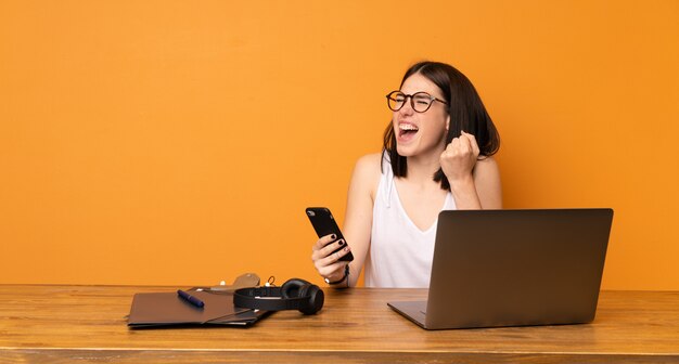 Bedrijfsvrouw in een bureau met telefoon in overwinningspositie