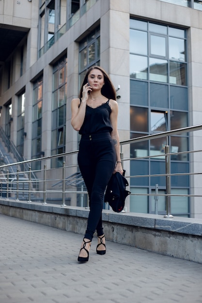 Bedrijfsvrouw Met Telefoon Dichtbij Bureau. Portret van mooie lachende vrouw In mode Office kleding praten over de telefoon terwijl je buiten staat. Telefonische communicatie. Hoge kwaliteit afbeelding.