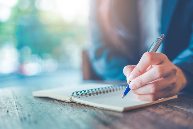 Bedrijfsvrouwenhand die op een blocnote met een pen in het bureau schrijven.