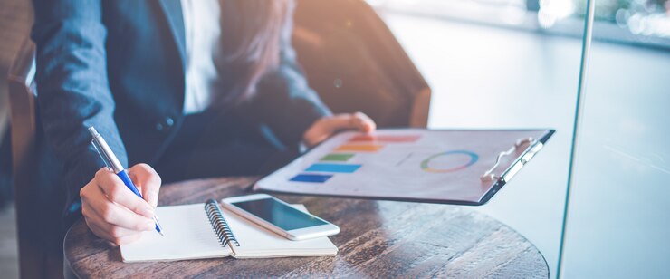 Bedrijfsvrouwenhand die op een blocnote schrijven en analysekaarten en grafieken gebruiken