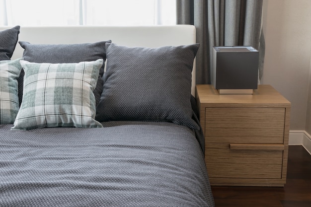 Дизайн интерьера спальни с проверенными зелеными подушками на серой кровати и декоративной настольной лампой.