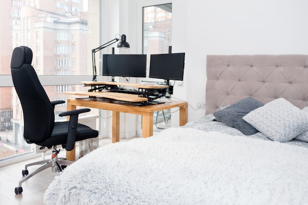 Bedroom interior with a study corner. Large double bed and a desk with a computer and a rolling chair.