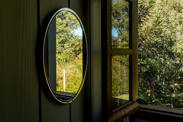 정원의 나무를 반사하는 거울이 있는 침실 창문.