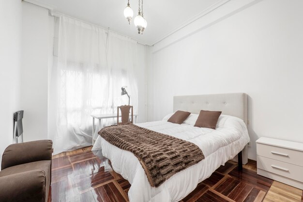 Foto camera da letto con letto con piumino bianco coperta marrone con cuscini coordinati tavolo da studio bianco e parquet in rovere