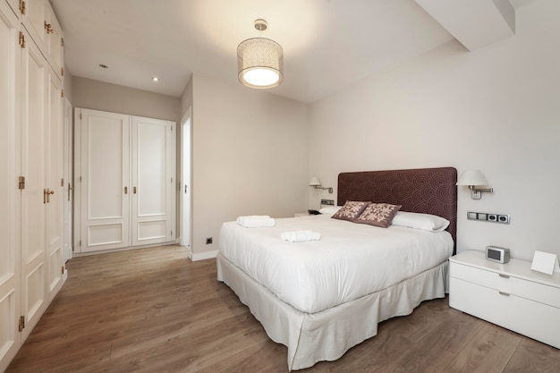 Bedroom with double bed with upholstered headboard white bedside tables fitted wardrobes with wooden doors and light wooden floors