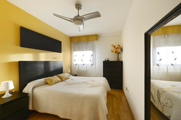 Спальня с двуспальной кроватью, желто-белыми стенами, зеркалами в черных рамах и соответствующей черной мебелью.