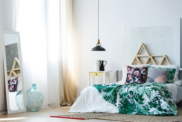 A bedroom with a green and white bedding and a black lamp hanging from the ceiling.