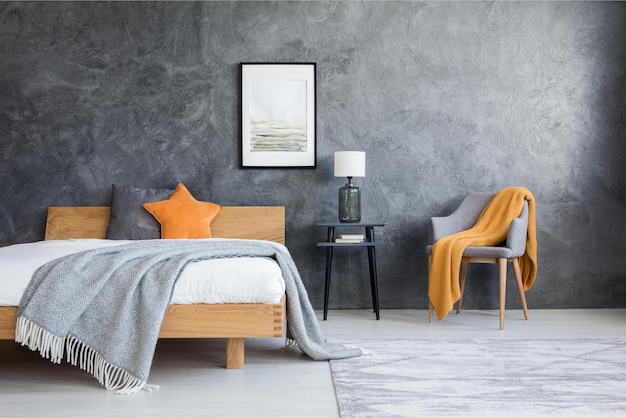 A bedroom with a grey wall and a bed with a orange blanket on it.