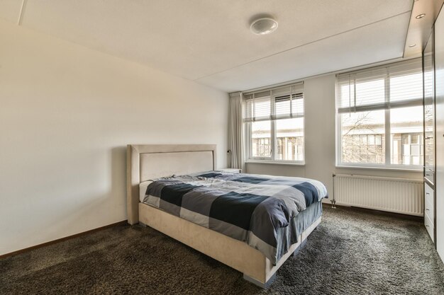 a bedroom with a large bed and two windows in the room all white walls are decorated with grey carpeting