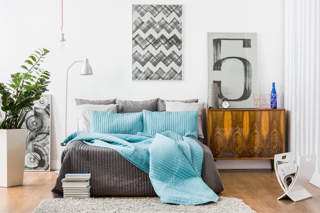 A bedroom with a large number of pillows on the bed and a lamp on the wall.