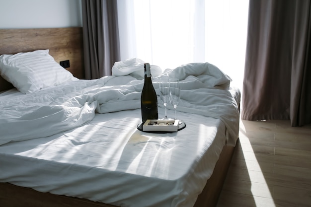 Camera da letto con un letto disteso lenzuola bianche sul letto con champagne e bicchieri estate il raggio di sole