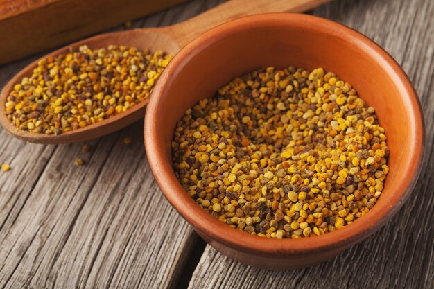 Bee pollen in bowl and wooden spoon on wooden background, copy space