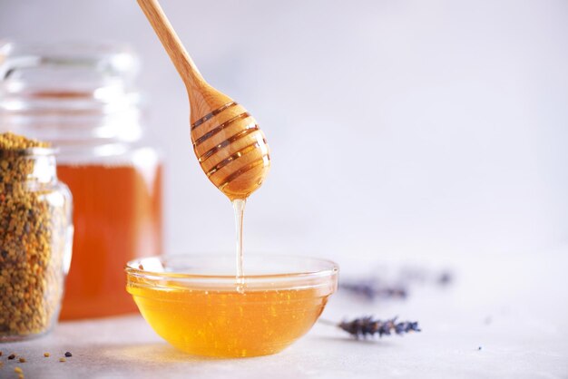 Bee pollen granules honey jar with wooden dropper honeycomb on grey backdrop copy space autumn harvest concept