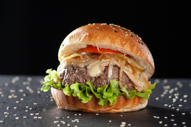 Photo beef burger with caramelized onion, lettuce, tomato on blackboard plate