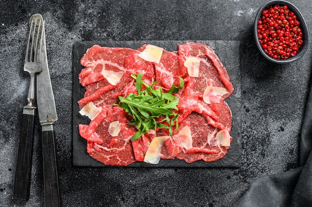 Beef carpaccio on black plate with parmesan cheese and arugula