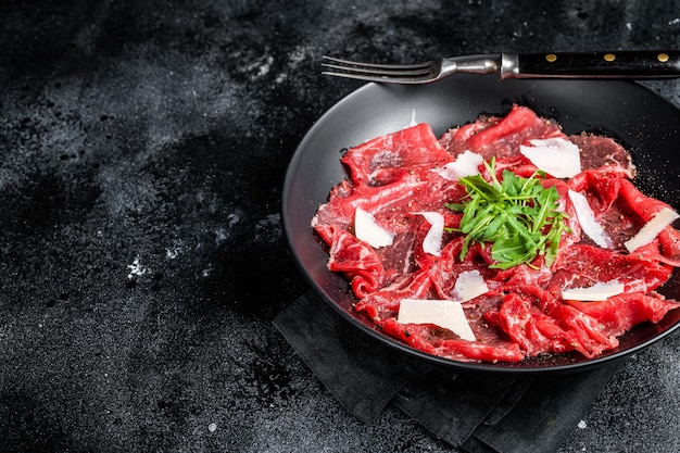 牛肉のカルパッチョ冷たい前菜、皿にパルメザン チーズとルッコラを添えて黒い背景上面図コピー スペース