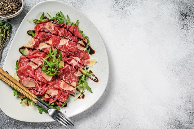 Photo beef carpaccio on white plate with parmesan cheese and arugula