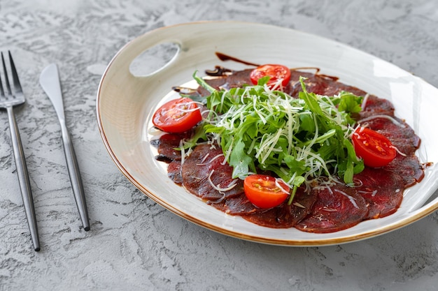 Beef carpaccio with arugula and parmesan on gray surface